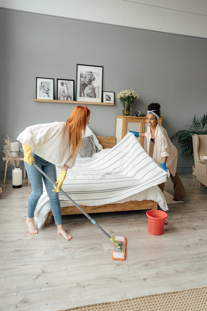 Two women mopping and tidying a modern bedroom, creating a cheerful vibe.